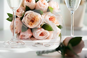 Wedding rings lie next to two glasses of champagne and a bouquet of roses