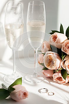 Wedding rings lie next to two glasses of champagne and a bouquet of roses