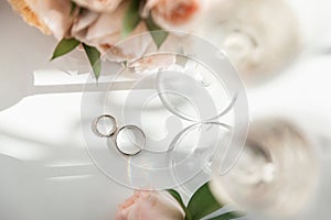 Wedding rings lie next to two glasses of champagne and a bouquet of roses