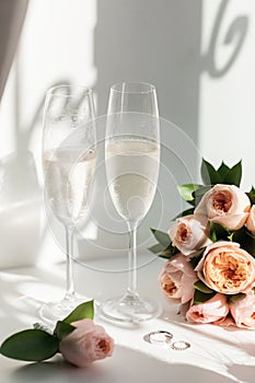 Wedding rings lie next to two glasses of champagne and a bouquet of roses