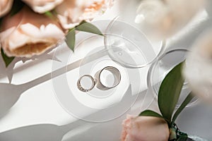 Wedding rings lie next to two glasses of champagne and a bouquet of roses