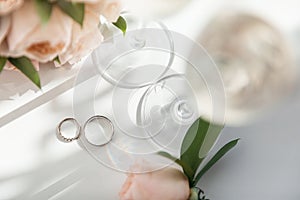 Wedding rings lie next to two glasses of champagne and a bouquet of roses