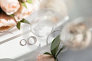 Wedding rings lie next to two glasses of champagne and a bouquet of roses