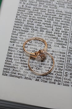 Wedding rings lie on the page of an open Bible. In the center of the ring the phrase is visible: God is Love