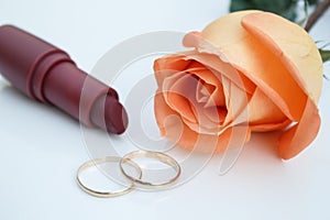 Wedding rings, lipstick and orange rose, on white background