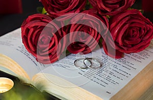 Wedding rings, red rose bouquet on open bible book for love and romance concept