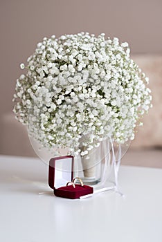 Wedding rings in a red velvet box and a bridal bouquet over a white table