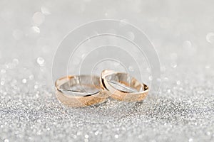 Wedding rings on a silver sparkling glitter background with bokeh