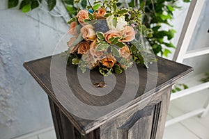 Wedding rings on a tinted wooden pedestal on the background of a stylish wedding bouquet