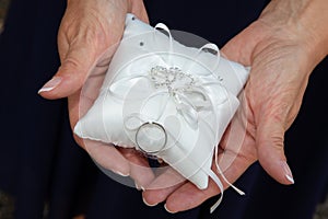 Wedding rings on white cushion over bride marriage hands