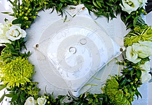 Wedding rings on a white cushion in a wreath of flowers