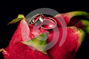Wedding rings white gold on an exotic fruit - close-up, black background