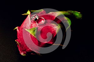 Wedding rings white gold on an exotic fruit - close-up, black background