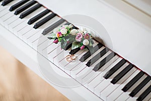 Wedding rings on white piano with flowers