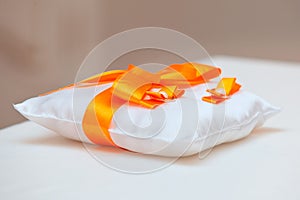 Wedding rings on a white pillow with orange ribbon