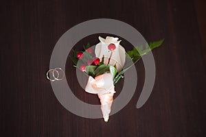 Wedding rings on a wooden table with the boutonniere in a vintage style