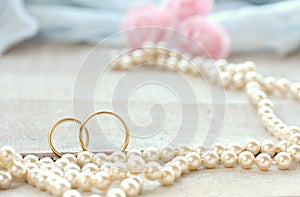 wedding rings on wooden white table, pearls beads, pink rose bouquet, selective focus