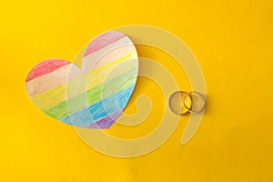 Wedding rings on a yellow background and a heart in the form of a flag lgbt, same-sex marriage, homosexuality