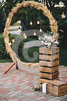 Wedding round arch in rustic style decorated with grass hay field color and retro light bulbs. Near the wooden boxes