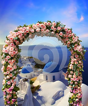 Wedding at Santorini. Beautiful arch decorated with flowers of roses with  blue church of Oia, Santorini, Greece at most romantic