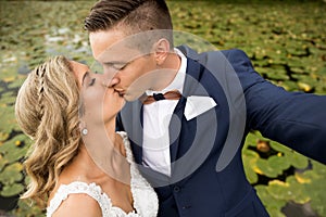 Wedding selfie. Bride and groom kissing passionately outdooors in park.