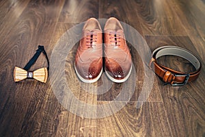 Wedding set of men's stylish shoes, wooden bow-tie and belt on a wooden background