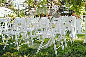 Wedding set up. Ceremony in the bosom of nature. White chairs with flowers set in the grass photo