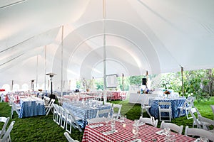 Wedding or special event tables set up for an outdoor barbeque with red and blue checkered table clothes under an event tent photo