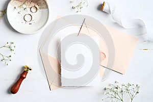 Wedding stationery on marble desk table. Blank wedding invitation card mockup, pastel pink envelopes, rings, wax seal stamp,