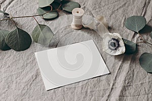 Wedding stationery mock-up scene. Blank greeting card on linen tablecloth background with white anemone flower