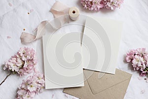 Wedding stationery mock-up scene. Blank greeting cards, envelope on linen tablecloth background with pink blossoming