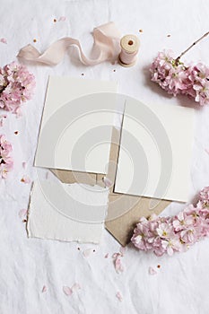 Wedding stationery mock-up scene. Blank greeting cards, envelope on linen tablecloth background with pink blossoming