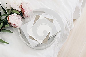 Wedding still life scene. Greeting card mockup scene, craft paper envelope, book on marble tray. Pink peony flowers on