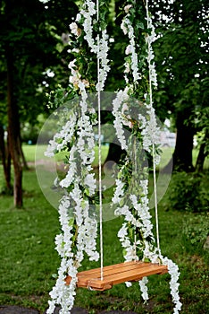 Wedding swing decorated with white flowers hanging on tree in garden, copy space.