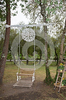 Wedding swing overgrown decorated with flowers hanging on the branches in the park