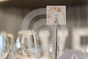 Wedding table with clear glasses topped with a card featuring white lettering that reads "Table 3"
