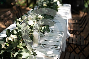 Wedding table decorated with white flower, candle in glass vase and green leaf on white tablecloth. composition of greenery. copy