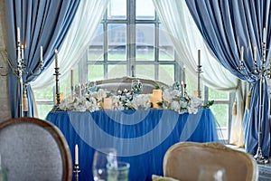 Wedding table decorated with white flowers, candles. Soft sofa with cushions, large window.Blue and white. photo