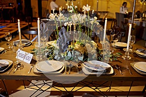 Wedding table dining set over white tablecloth, golden and white plates with floral arrengement