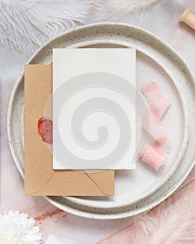 Wedding Table place with a card over envelope near flowers and feathers, mockup