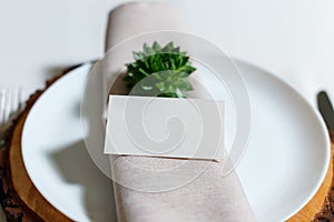 Wedding table setting with blank guest card, napkin, succulent on wooden plate. Rustic decor