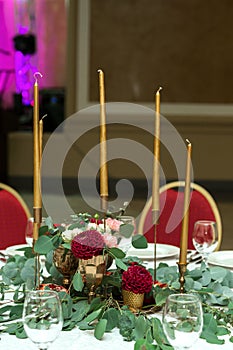 The wedding table setting is decorated with fresh flowers in a brass bowl and golden candles in brass candlesticks. Wedding