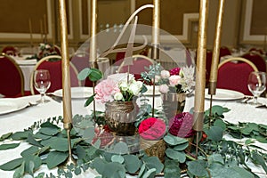 The wedding table setting is decorated with fresh flowers in a brass bowl and golden candles in brass candlesticks. Wedding