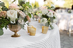 Wedding table setting decorated with fresh flowers in a brass vase. Wedding floristry. Banquet table for guests outdoors with a