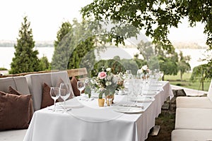 Wedding table setting decorated with fresh flowers in a brass vase. Wedding floristry. Banquet table for guests outdoors with a photo