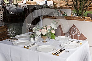 Wedding table setting decorated with fresh flowers in a brass vase. Wedding floristry. Banquet table for guests outdoors with a