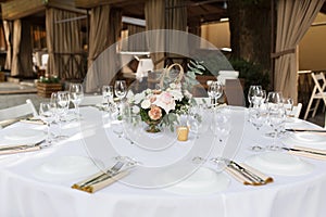 Wedding table setting decorated with fresh flowers in a brass vase. Wedding floristry. Banquet table for guests outdoors with a