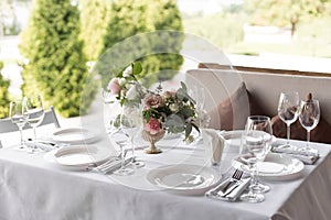 Wedding table setting decorated with fresh flowers in a brass vase. Wedding floristry. Banquet table for guests outdoors with a