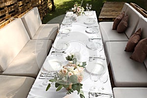 Wedding table setting decorated with fresh flowers in a brass vase. Wedding floristry. Banquet table for guests outdoors with a