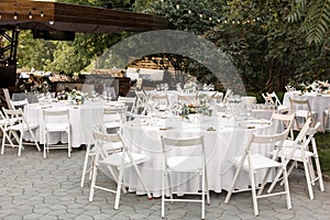 Wedding table setting decorated with fresh flowers in a brass vase. Wedding floristry. Banquet table for guests outdoors with a